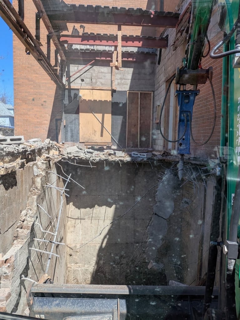 Abandoned brick building under demolition with exposed structural beams and concrete pit in debris-filled courtyard